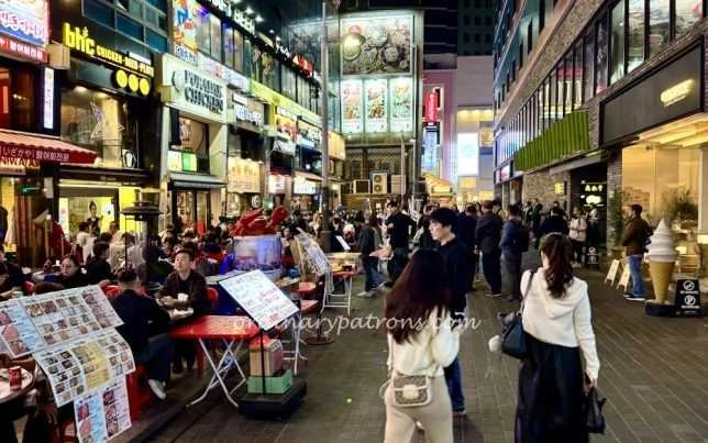 BHC明洞本店所在街道夜间实景，可认左上方招牌；不是当前排队长度。